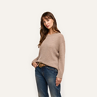 A woman wears a relaxed-fit, beige long-sleeved mid-weight Laine Cashmere Pullover tucked into blue jeans with a decorative belt.