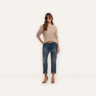 A woman wearing a relaxed fit beige long-sleeved Laine Cashmere Pullover, cuffed blue jeans with a belt, and tan heels, standing against a plain background.