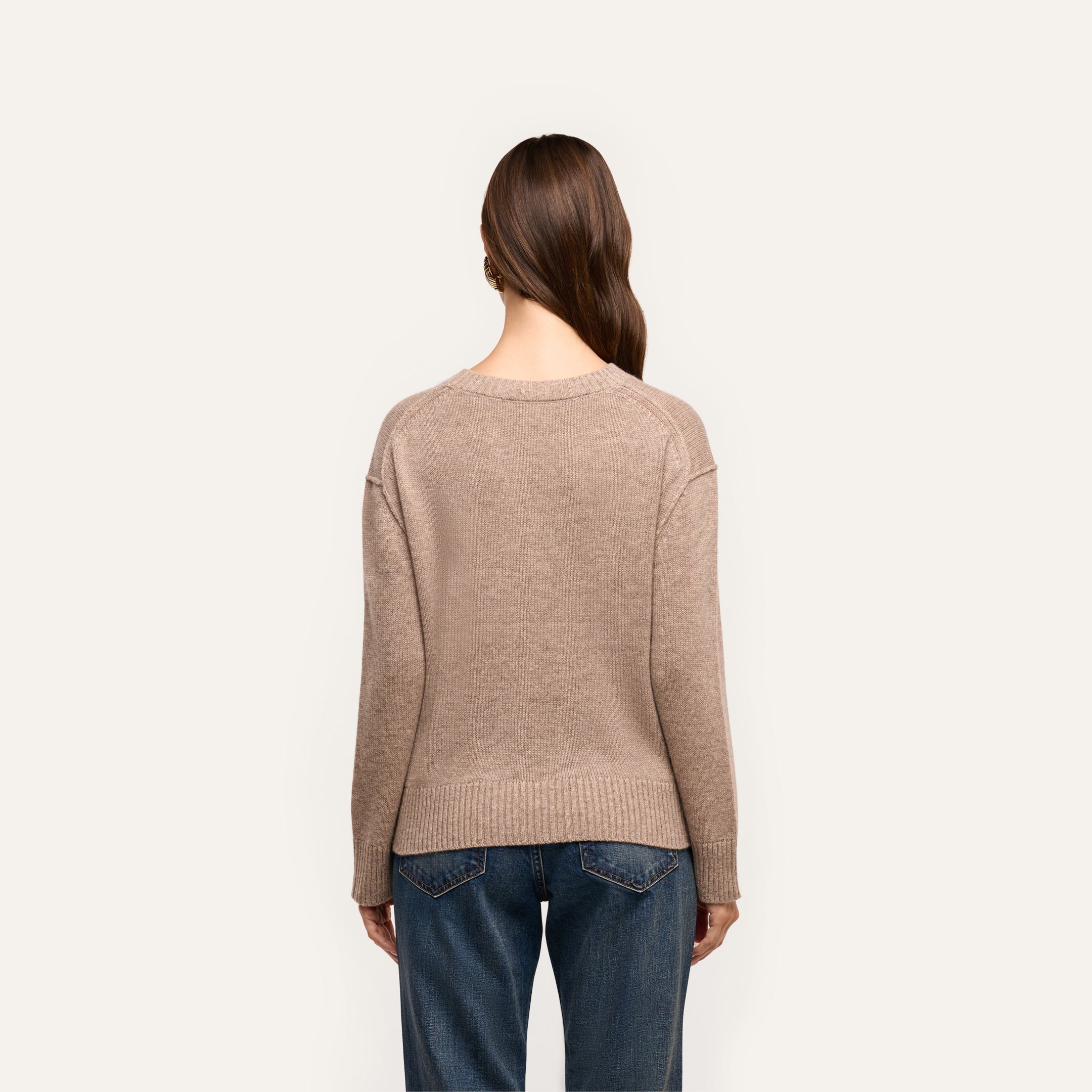 Back view of a person wearing a beige, relaxed fit Laine Cashmere Pullover and blue jeans.