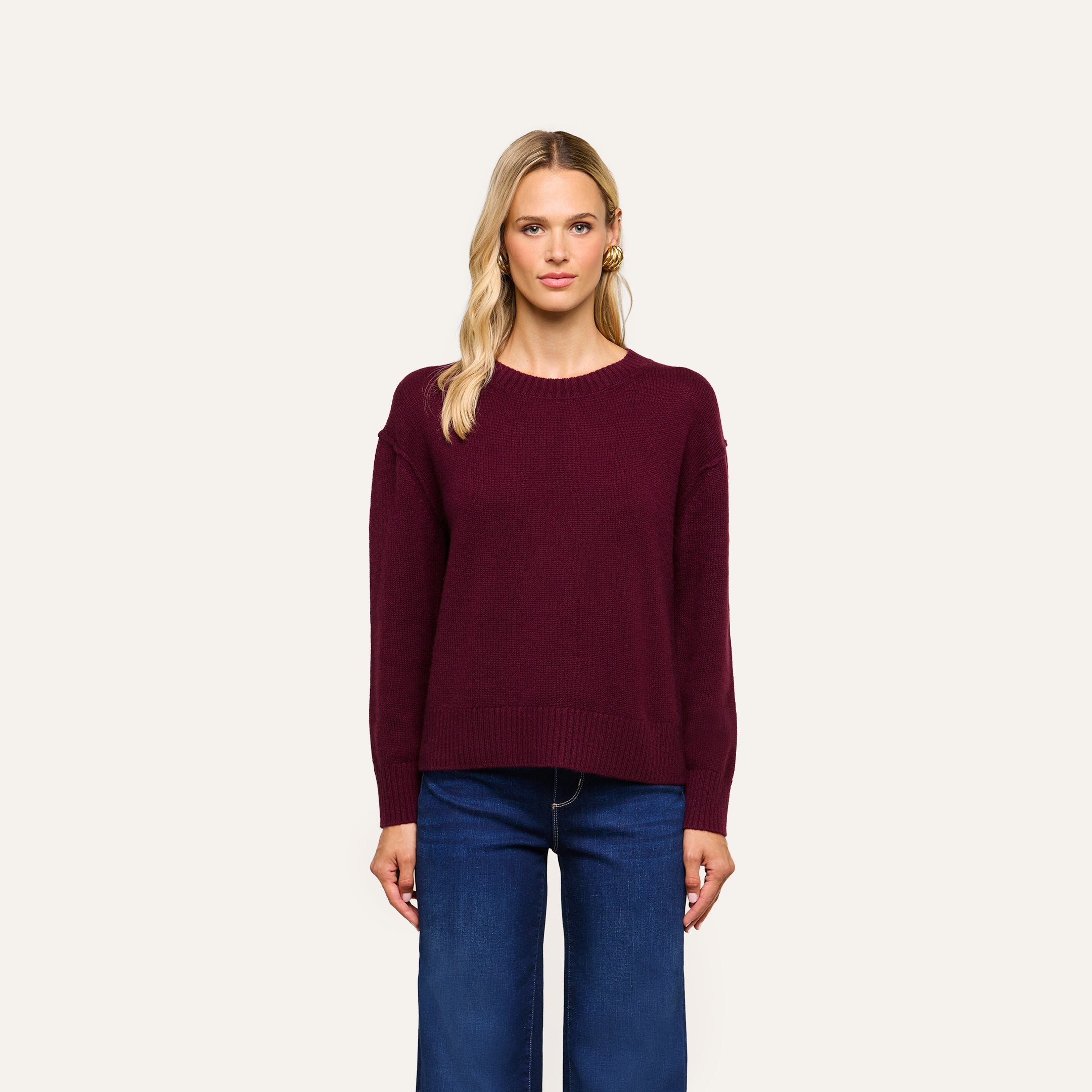 A woman with blonde hair wears the Laine Cashmere Top in a relaxed fit and blue jeans, standing against a plain light background, looking straight at the camera with a neutral expression.