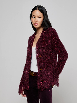 A woman with long black hair wears the L'AGENCE Azure Fringe Cardigan Blazer in burgundy over a white top and matching burgundy pants, standing against a plain light gray background.