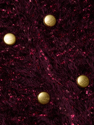 Four gold buttons engraved with L'AGENCE adorn the textured, deep burgundy eyelash knit of the Azure Fringe Cardigan Blazer, their shine contrasting beautifully against the richly colored, flecked background.