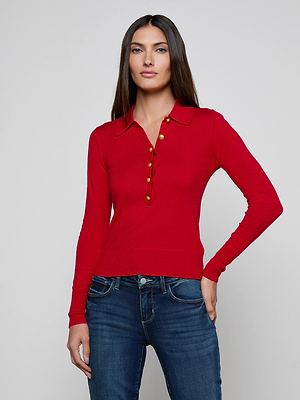 A woman with long straight hair wears the L'AGENCE Sterling Sweater, a slim fit, red henley-style top with gold buttons, paired with blue jeans and standing against a plain light gray background.
