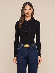 Wearing the Sterling Sweater, a woman with long brown hair pairs it with dark blue jeans and a wide black belt featuring a gold buckle, standing against a plain light background.