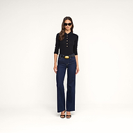 A woman wearing the Sterling Sweater, a black long sleeve knit top, along with dark blue high-waisted jeans, black sandals, sunglasses, and a wide belt stands against a plain white background.