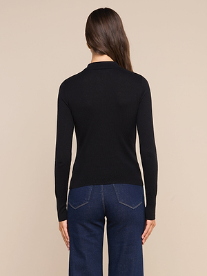 A woman stands with her back to the camera, wearing the Sterling Sweater and dark blue jeans against a plain beige background.