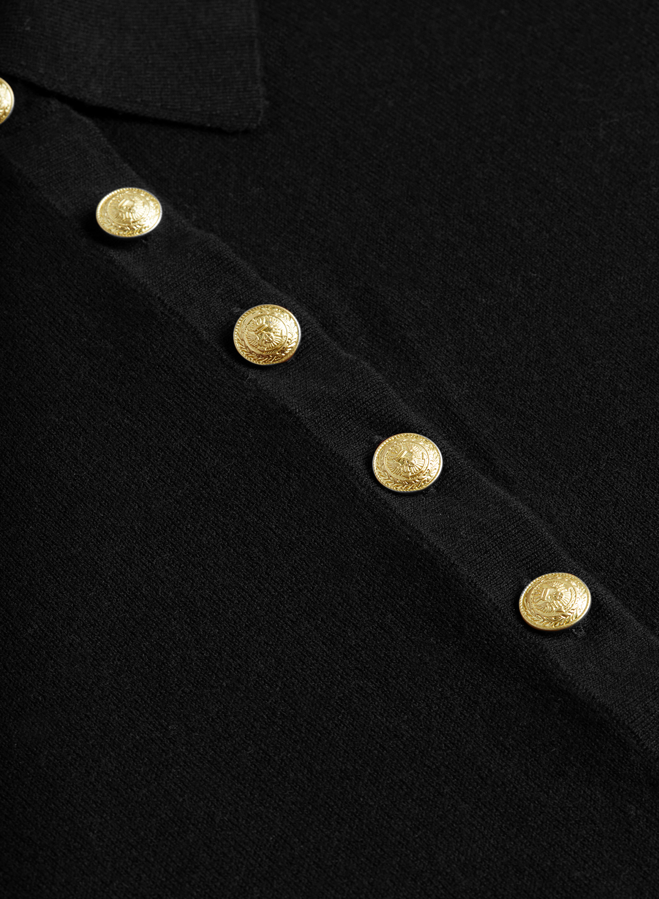 Close-up of the Sterling Sweater in black, featuring five gold decorative buttons arranged vertically. Each button is embossed with intricate designs, lending a classic and elegant touch to the fabric.