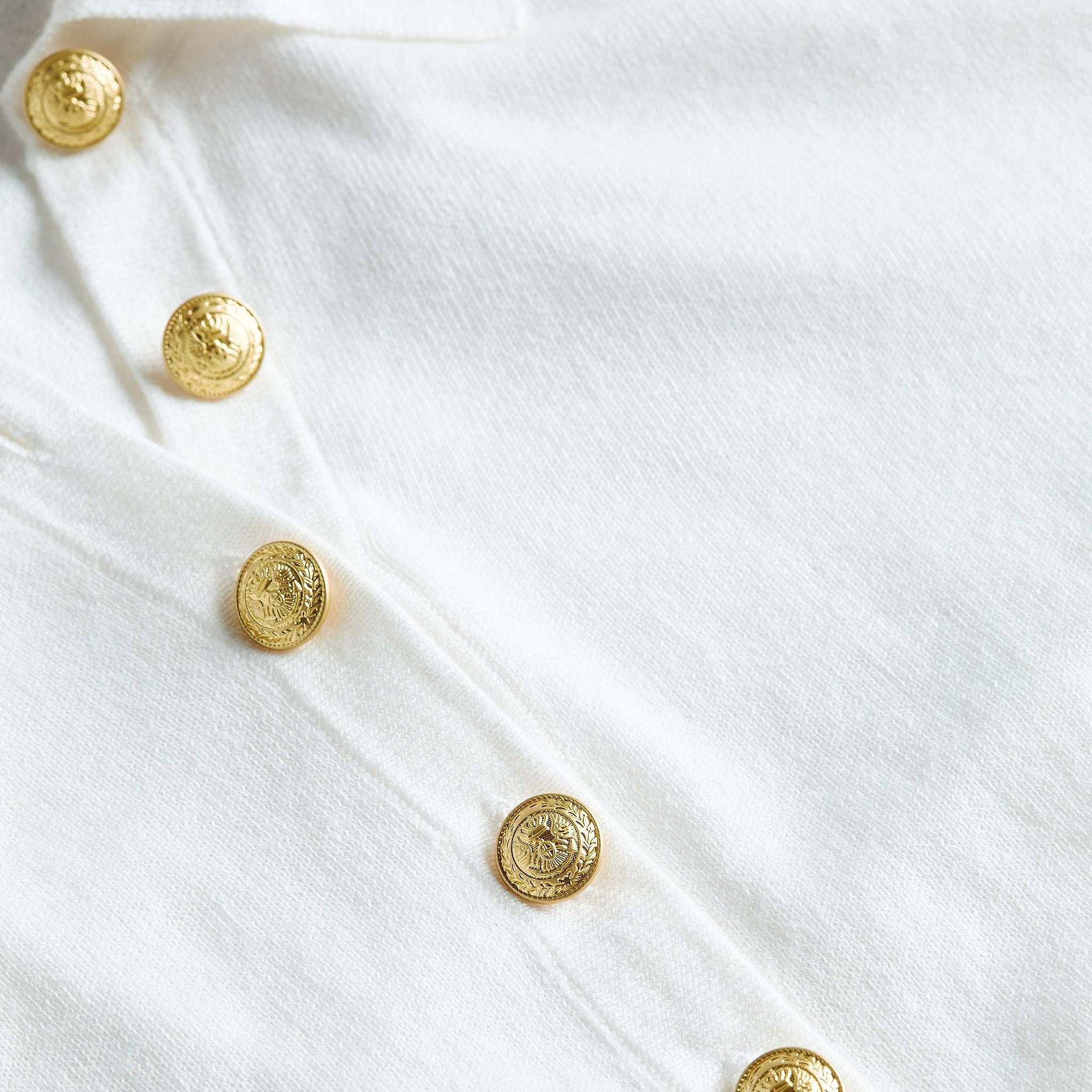 Close-up of the Sterling Sweater, crafted from premium white knit fabric, showcasing a slim fit silhouette and adorned with a row of gold decorative buttons featuring embossed details.