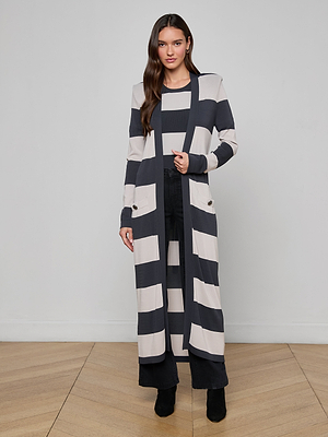 A woman faces the camera wearing the Berlin Duster Cardigan with wide horizontal stripes, paired with black pants and boots, against a plain light gray background.