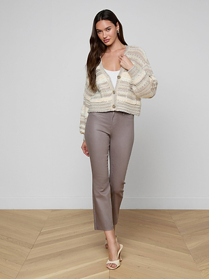 A woman poses indoors wearing the Harriet Cardigan with blouson sleeves over a white top, taupe cropped pants, and beige heeled sandals. She stands on a wooden floor against a plain white wall.