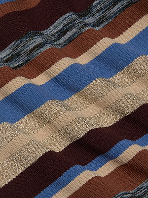 A close-up of the Olene Turtleneck by L'AGENCE, featuring ribbed knit fabric with wavy horizontal stripes in brown, blue, beige, tan, and metallic gold for an abstract, textured look.