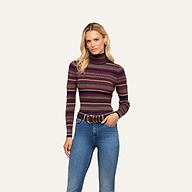 A woman with long blonde hair wears the Olene Striped Turtleneck, paired with blue jeans and a brown belt. She stands against a plain light background, one hand in her pocket and a neutral expression, showcasing effortless fall style.