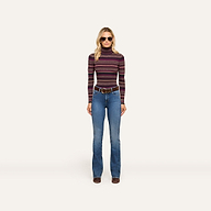 Wearing the Olene Striped Turtleneck with blue flared jeans, a wide brown belt, brown shoes, and stylish sunglasses, the woman stands against a plain light background—an effortless nod to classic fall fashion.
