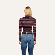 Wearing the Olene Striped Turtleneck in maroon and purple stripes paired with blue jeans, a person with long blonde hair stands facing away from the camera against a plain light background—an effortlessly stylish look ideal for fall fashion.