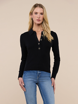 A woman with long blonde hair wears the Sterling Sweater, a black, long-sleeve knit collared sweater with floral buttons, paired with slim fit light blue jeans. She stands facing forward against a plain beige background.