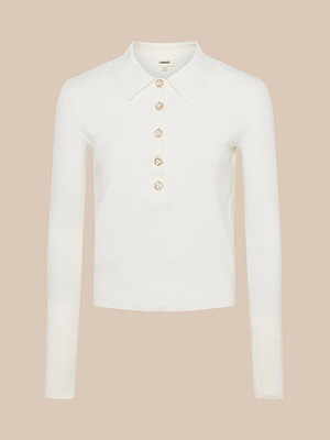 The Sterling Sweater is a slim fit, long sleeve white knit top featuring a pointed collar and four decorative pearl-like buttons down the front, shown on a plain beige background.