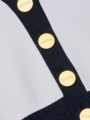 Close-up of the Taya Cardigan, a black and white Parisian-style piece featuring a vertical row of shiny gold buttons engraved with LAGENCE PARIS on the black section, giving it an elegant metallic accent.