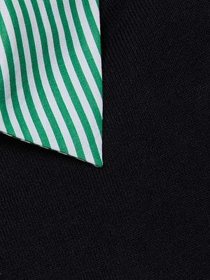 A close-up shows the pointed end of a green and white striped tie beside the crisp collar of the April Poplin Collar Pullover, both resting on a dark textured fabric.
