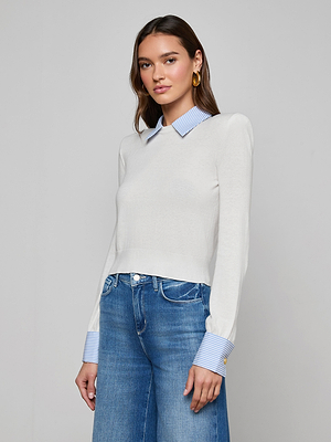 A woman wears the April Poplin Collar Pullover—an ultra-light white knit top with blue-and-white striped poplin collar and cuffs—paired with blue jeans, posing against a plain light gray background.