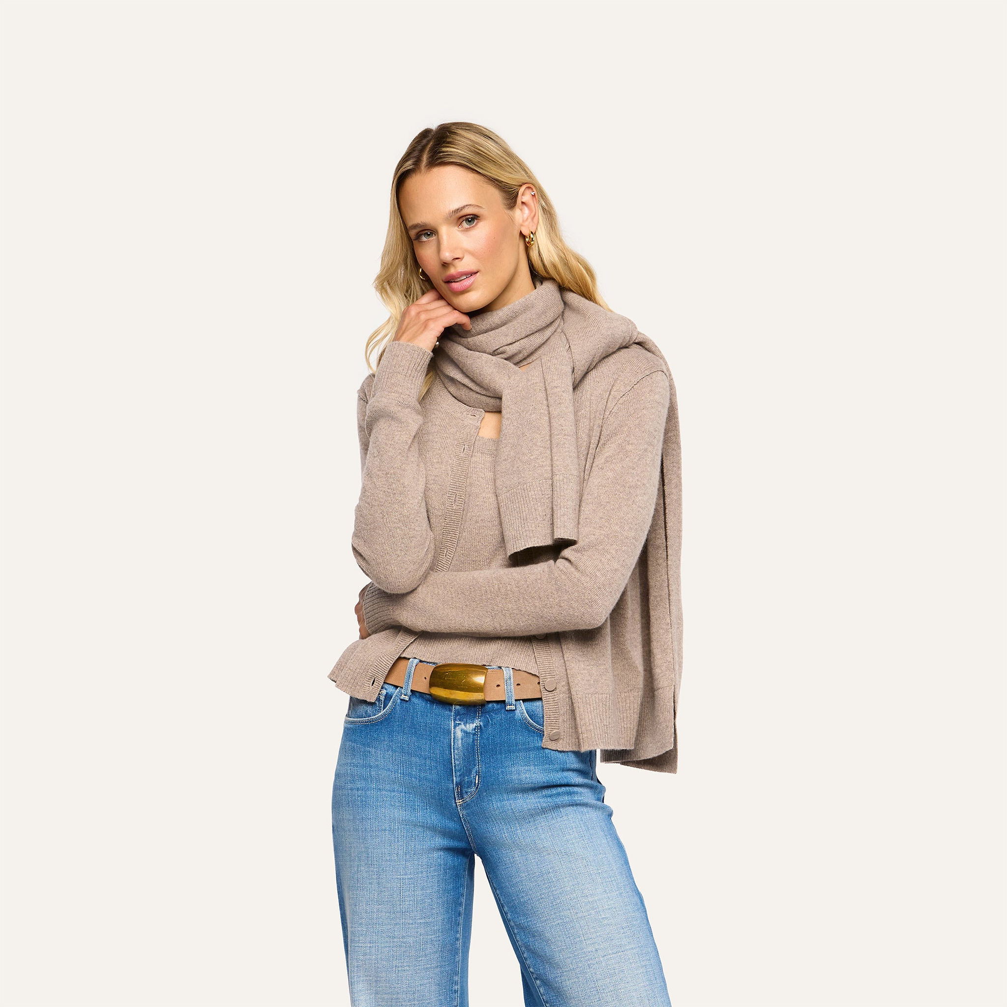 A woman wearing a pebbled tan Palais Cashmere Scarf draped over a matching sweater and blue jeans.