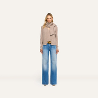A woman wearing a tan Palais Cashmere Scarf draped over a matching cardigan and tank top with blue wide-leg jeans.