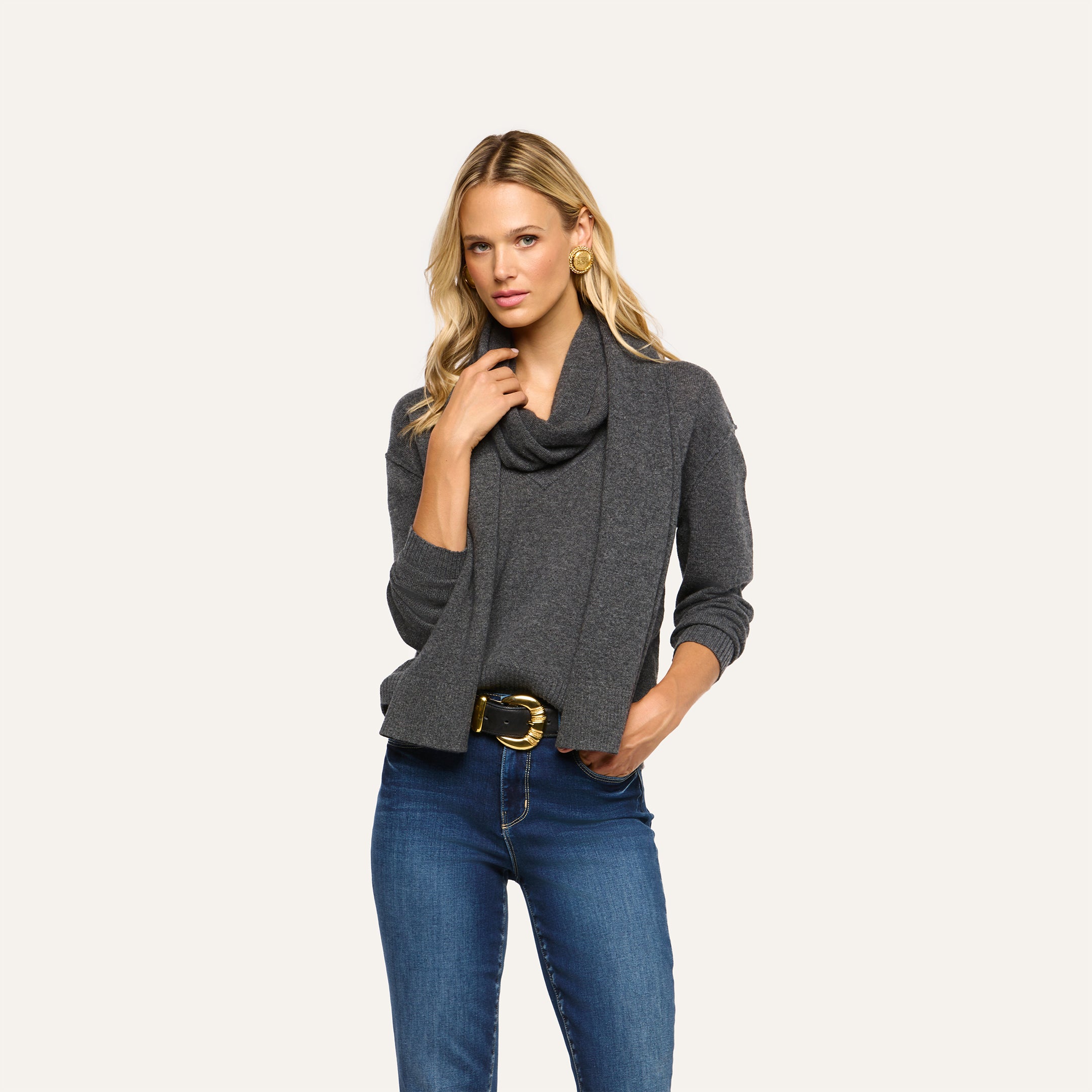A woman wearing a charcoal gray Palais Cashmere scarf draped over a matching gray long-sleeved sweater and blue jeans.