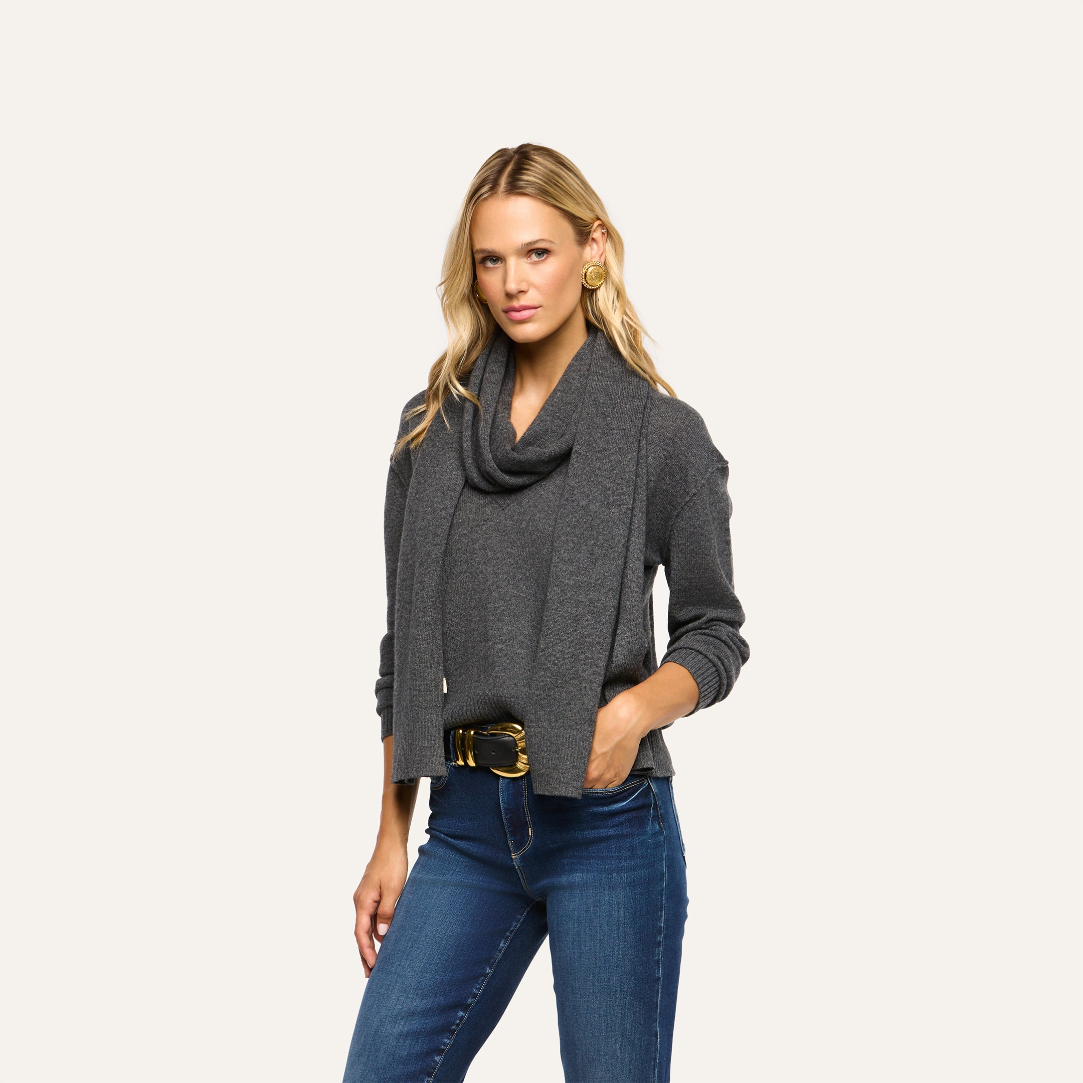 A woman wearing a charcoal grey Palais Cashmere Scarf draped over a matching long-sleeve sweater and blue jeans.