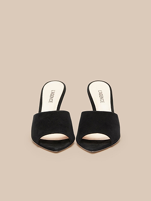 The Lolita Suede Open-Toe Mule is a pair of black suede, slip-on heels with beige insoles, shown on a neutral beige background.