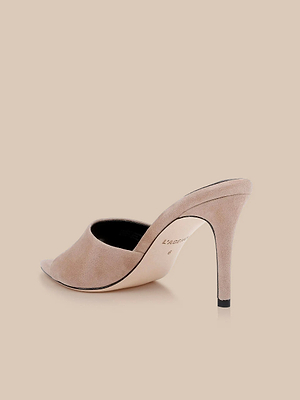 The Lolita Suede Open-Toe Mule features cappuccino suede, an open toe, and a slim stiletto heel, displayed against a coordinating beige background.