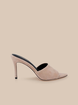 The Lolita Suede Open-Toe Mule is a high-heeled, slip-on shoe in cappuccino suede with a black inner sole and open toe, displayed against a matching beige background.