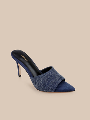 The Lolita Denim Open-Toe Mule is a chic womens heel featuring a pointed toe, denim upper wide strap, and sleek black insole, showcased against a beige background.