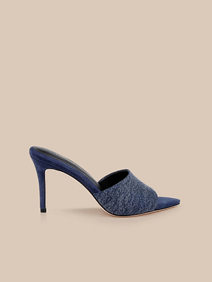 The Lolita Denim Open-Toe Mule, featuring a blue denim upper and slim heel, is showcased against a plain beige background.