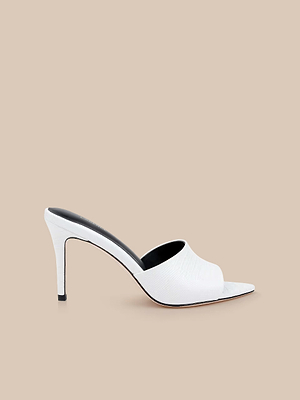 The Lolita Leather Open-Toe Mule, featuring a lizard-embossed white leather finish, is displayed against a plain beige background, highlighting its chic minimalist style.