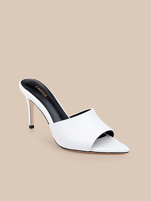 The Lolita Leather Open-Toe Mule is a white lizard-embossed peep-toe shoe featuring a textured upper, black insole, and slim stiletto heel, showcased on a beige background for a chic minimalist look.