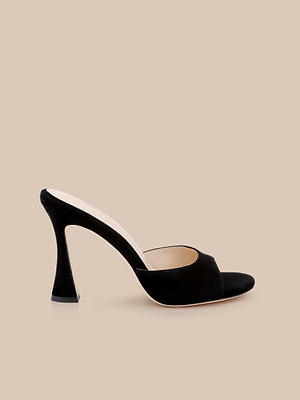 The Avery Suede Open-Toe Mule is a sculpted stiletto mule in black suede with a wide strap, showcased elegantly on a beige background.