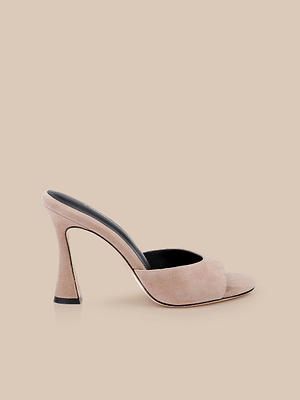 The Avery Suede Open-Toe Mule features a beige sculpted stiletto heel, wide cappuccino suede strap, black insole, and open toe, shown against a matching beige background.