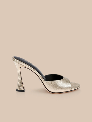 The Avery Leather Open-Toe Mule, featuring gold textured leather and a flared heel, is displayed on a beige background.