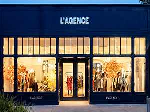 Storefront of L'Agence with illuminated interior displaying clothing and decor.