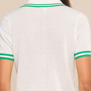 A person wearing a white knit short-sleeve shirt with green trim on the sleeves and collar, shown from the back.