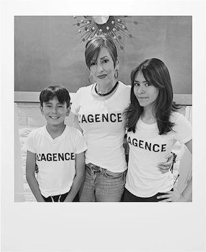 A woman and two children stand together, all wearing matching white T-shirts with LAGENCE printed on them. The photo is in black and white. The woman is in the center with her arms around the children.