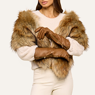 A woman with her arms crossed showcases the Carmen Gloves—luxurious leather gloves—paired with a beige sweater and a faux fur shawl. Only her lower face is visible against a plain, light-colored background.