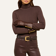 Woman wearing brown leather Tosca Gloves with gold buttons, styled with a brown turtleneck, brown leather pants, and a brown belt featuring a gold buckle, standing with arms crossed against a plain background.