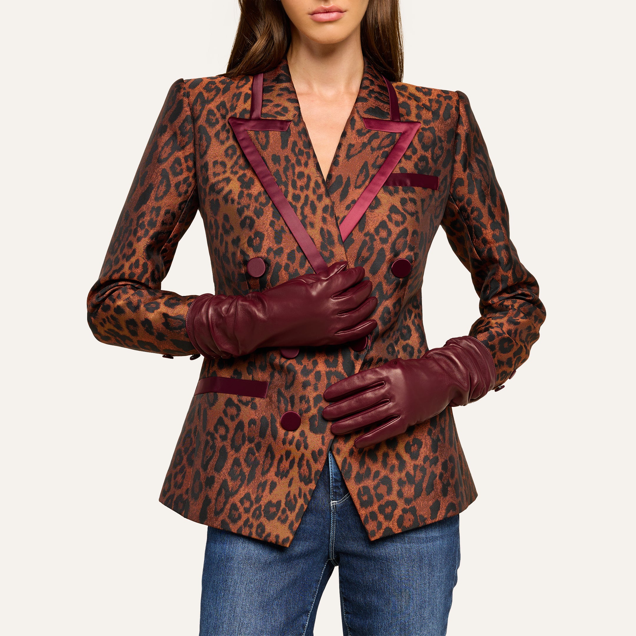 A woman wearing blue jeans, a leopard print blazer with burgundy trim, and the luxurious Boheme Gloves crafted from lambskin leather stands against a plain light background.