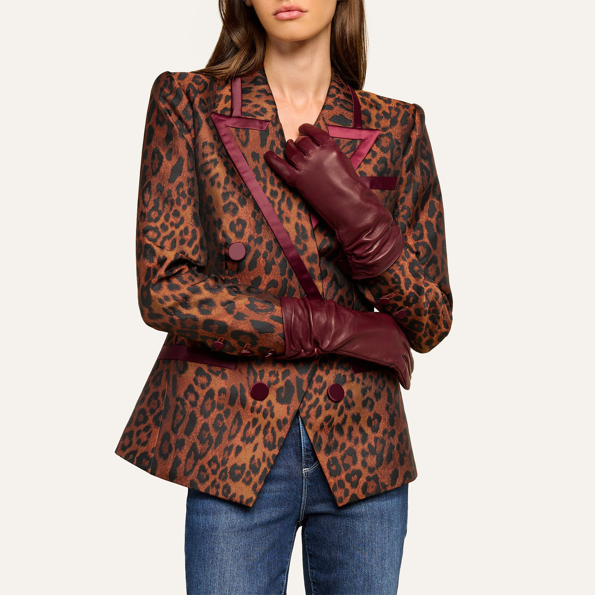 Woman wearing a leopard print blazer with burgundy trim and buttons, styled with the luxe Boheme Gloves in burgundy leather and blue jeans. Her hair is down and her face is partially out of frame.