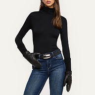 A woman stands with one hand on her hip against a plain background, wearing a black turtleneck, blue jeans, a black belt, and the Tempo Mittens. Her face is partially visible.