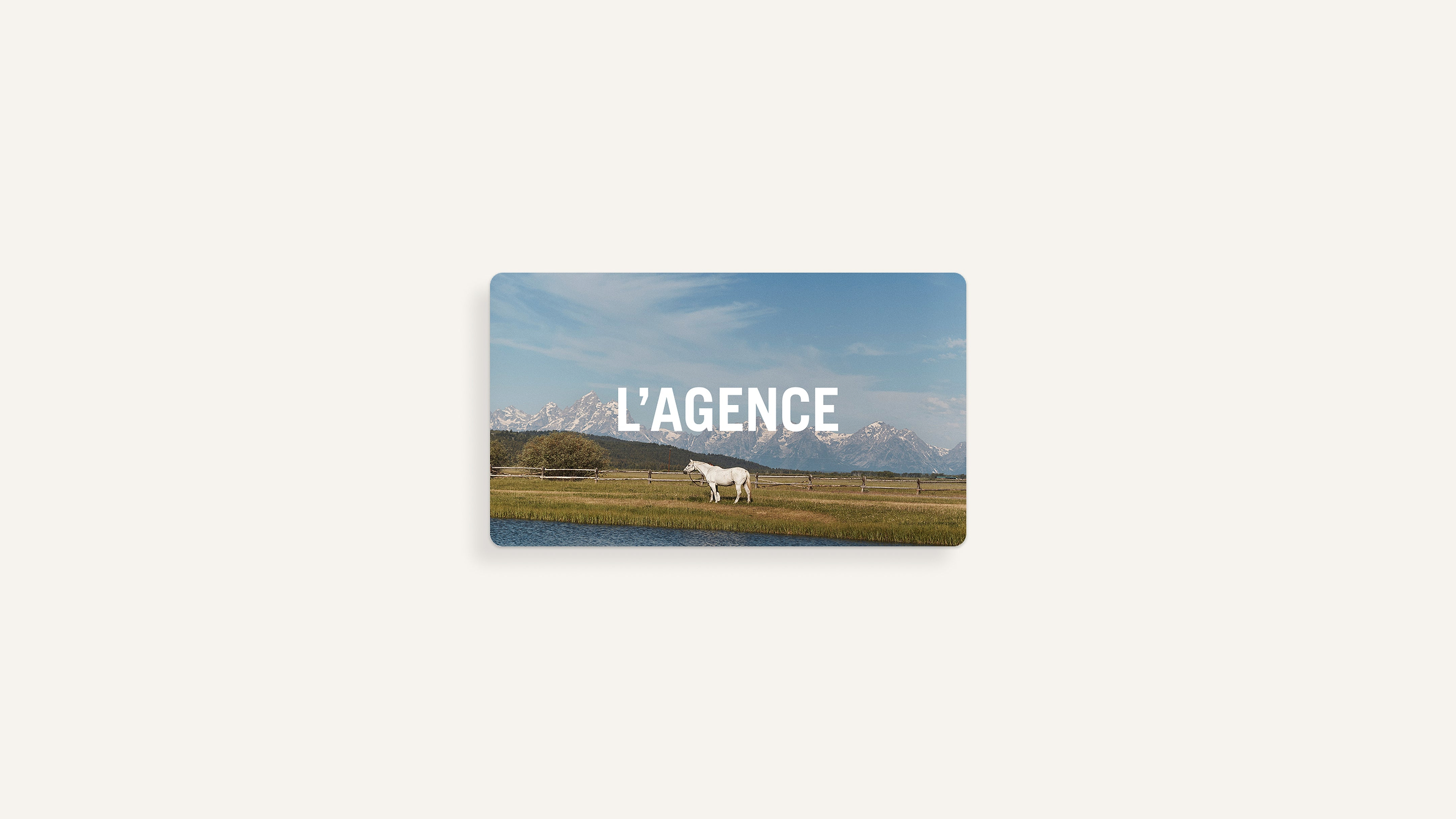 A white horse stands on grass by water, with snowy mountains in the background and LAGENCE in bold white text across the middle.