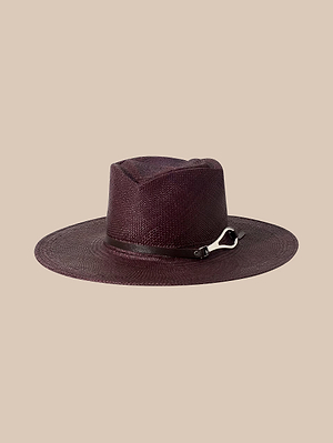 Le chapeau Estella Fedora est un chapeau de paille à large bord, de couleur bordeaux foncé « espresso », fabriqué à la main à Los Angeles. Il est orné dun ruban assorti rehaussé dune boucle métallique, présenté ici sur un fond beige uni.