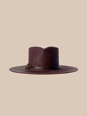 Le chapeau Estella Fedora est un chapeau de paille couleur espresso à large bord, au sommet plat et orné dun ruban en cuir marron. Fabriqué à la main à Los Angeles, il est présenté ici sur un fond beige.