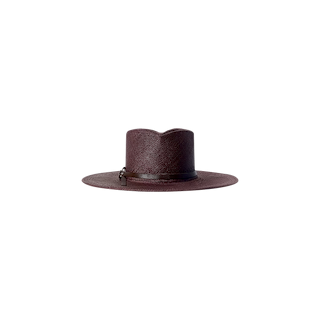 The Estella Fedora is a wide-brimmed hat crafted from textured material in a deep burgundy shade, featuring a subtle leather band encircling the crown. Handcrafted in LA, it is showcased against a plain white background.
