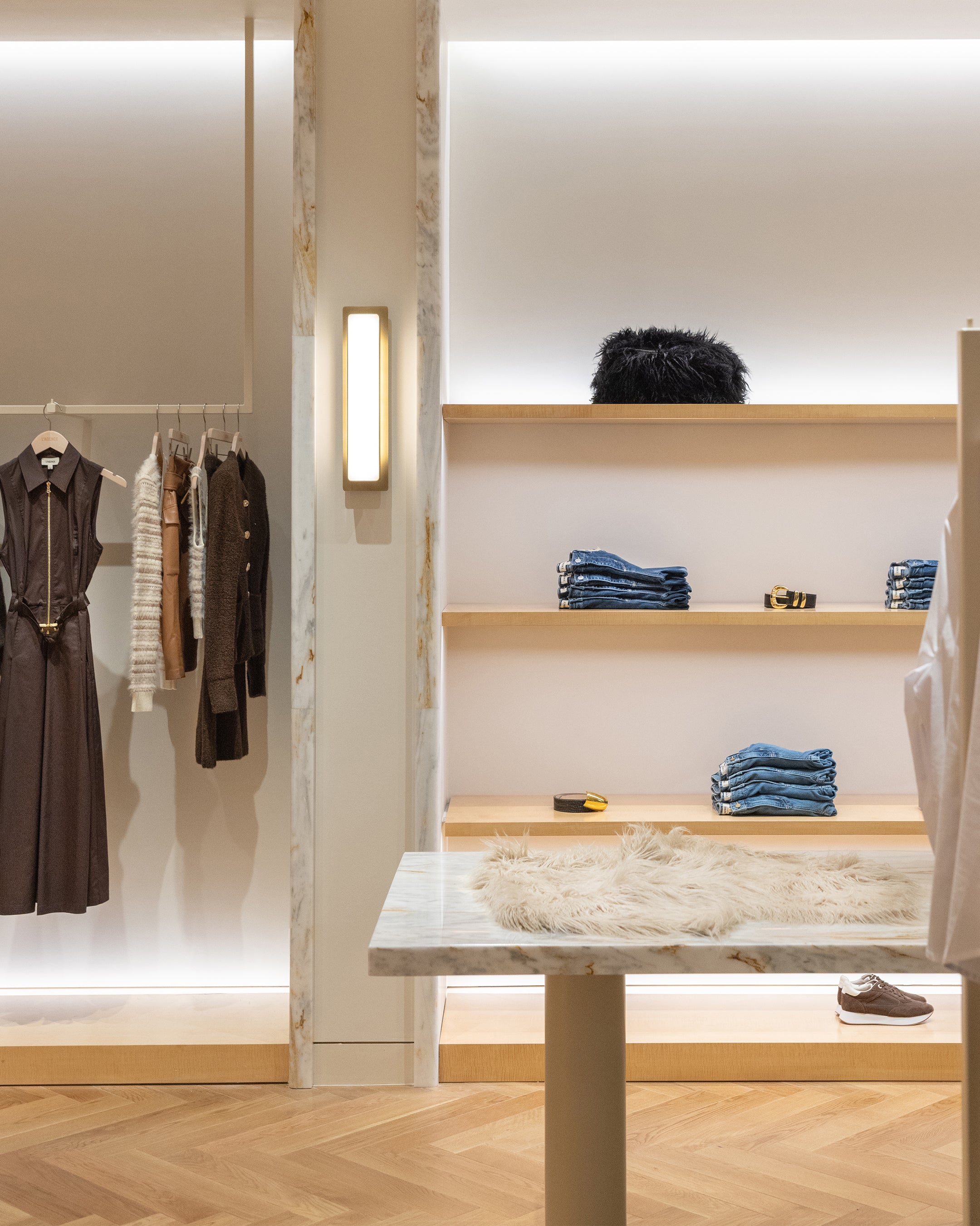 Clothing rack with dresses and sweaters beside tiered shelves displaying folded denim, a belt, and accessories in a boutique retail store.